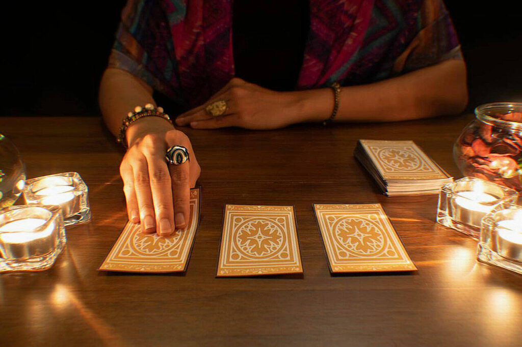 Hands laying out tarot cards beside a lit candles